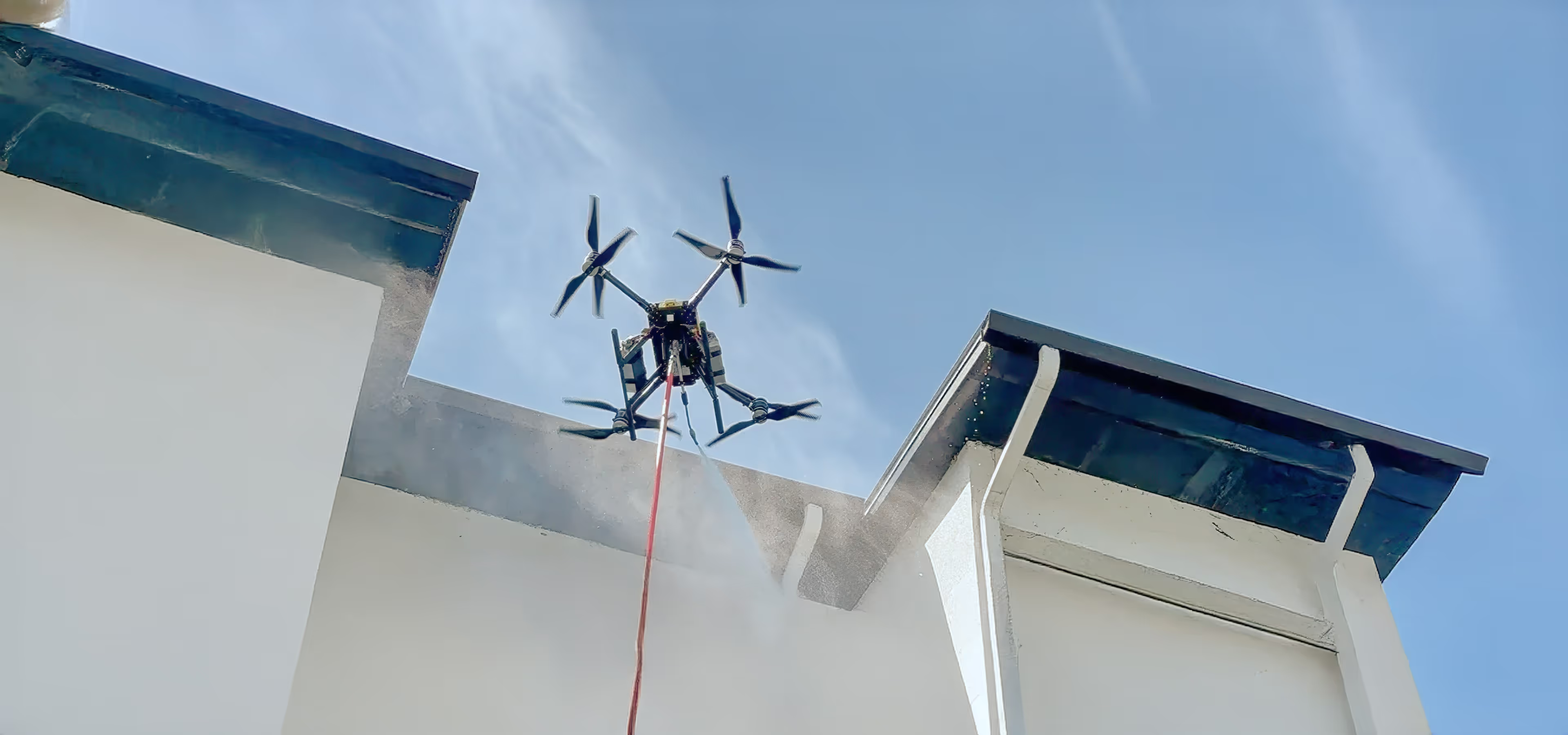 A drone cleaning the exterior of a commercial building using a high-pressure spraying system.
